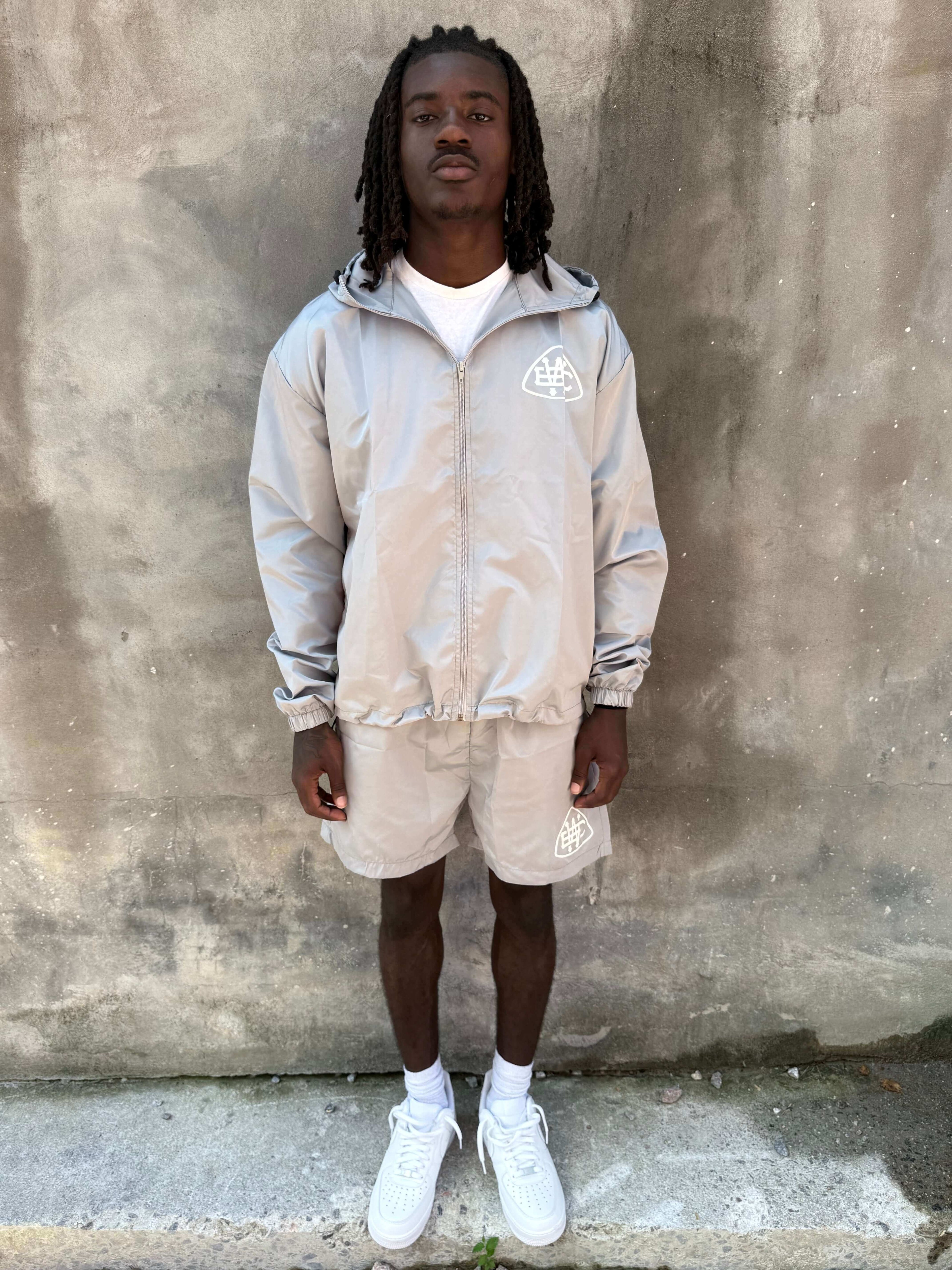 Model wearing Grey Unerring Set featuring drawstring hood, elastic cuffs, and bold white logo on shorts.