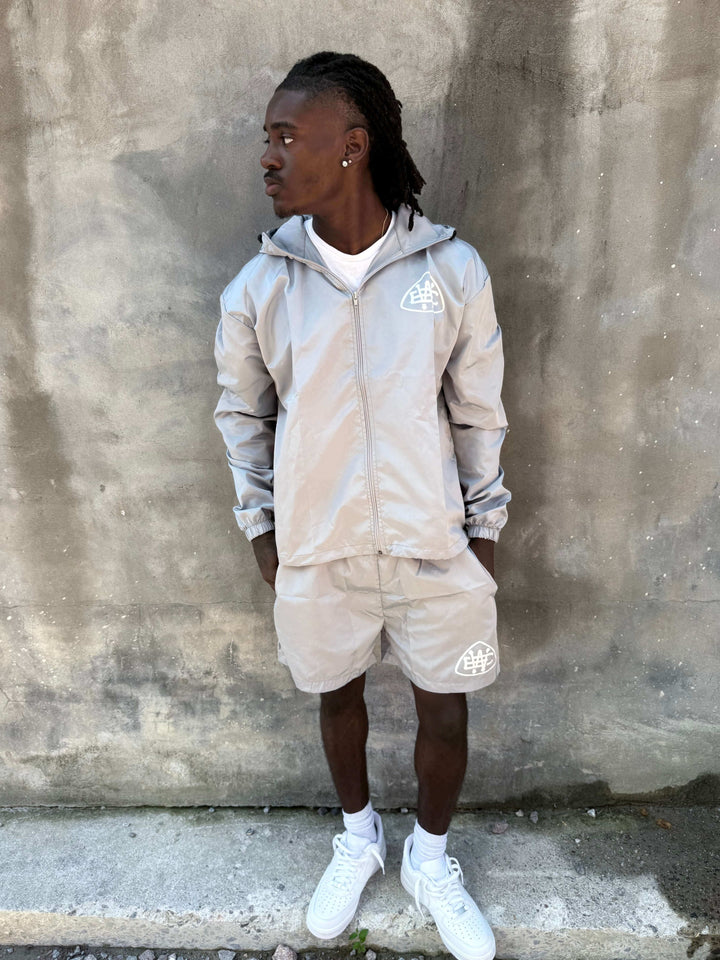 Model wearing Grey Unerring Set with drawstring hood, elastic cuffs, and bold logo, styled with white sneakers.
