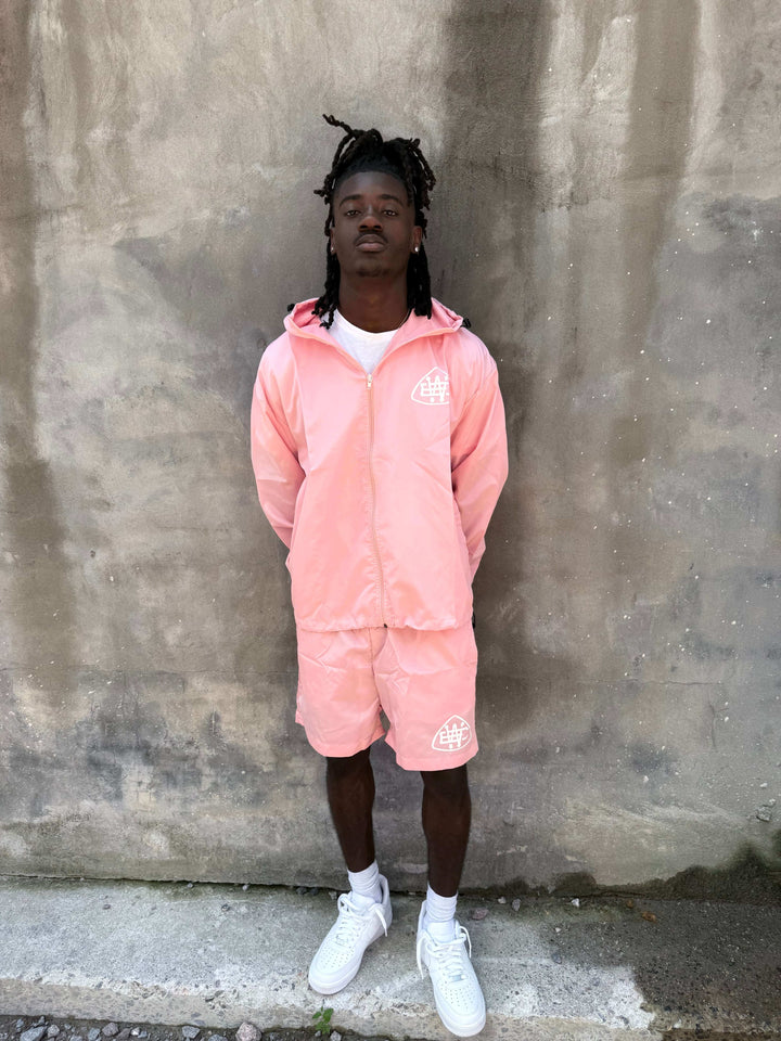Model wearing pink unerring set with drawstring hood, elastic cuffs, and bold logo, perfect for stylish casual wear.