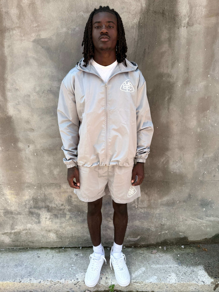 Model wearing Grey Unerring Set featuring drawstring hood, elastic cuffs, and bold white logo on shorts.