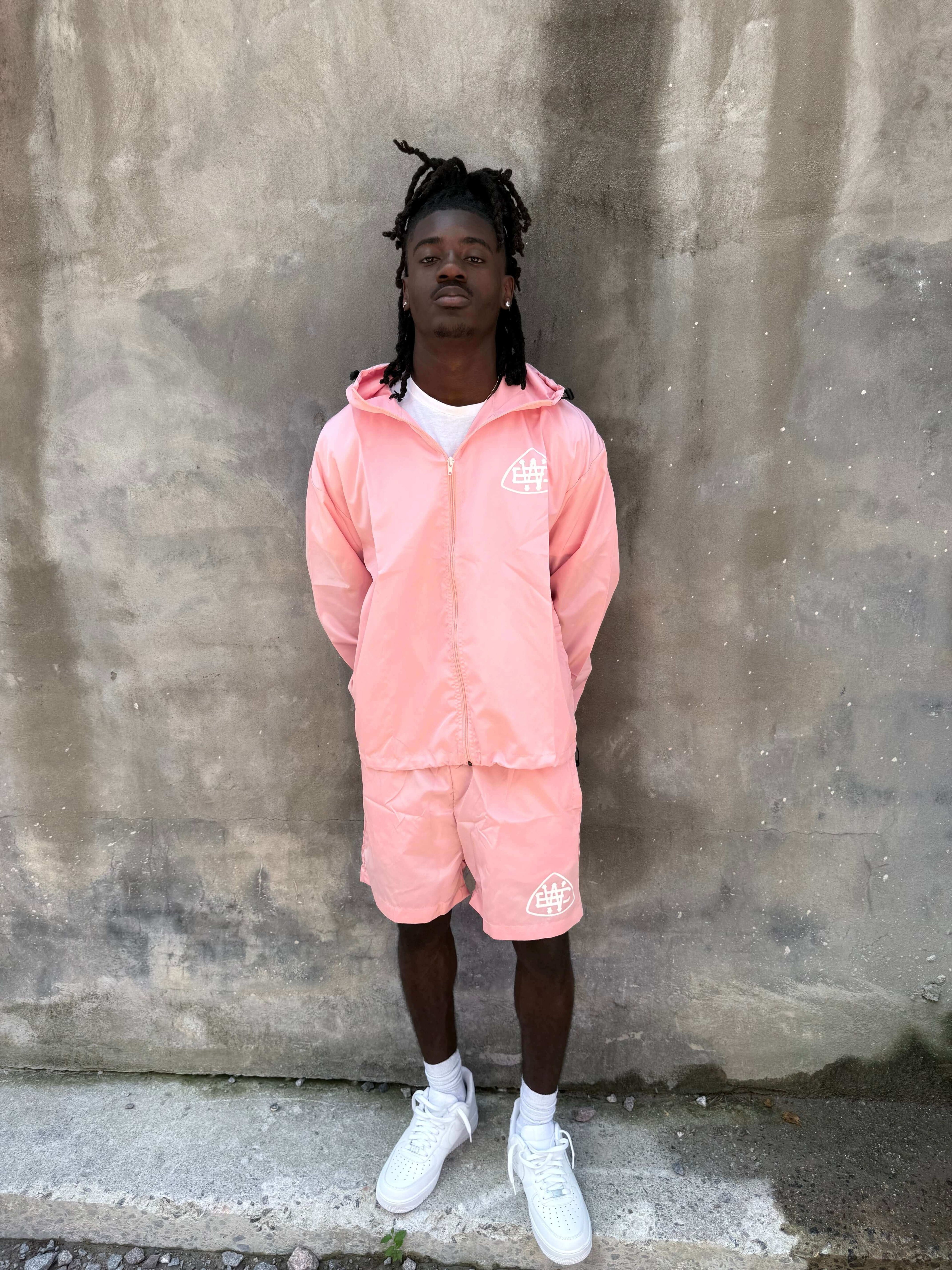 Model wearing pink unerring set with drawstring hood, elastic cuffs, and bold logo, perfect for stylish casual wear.